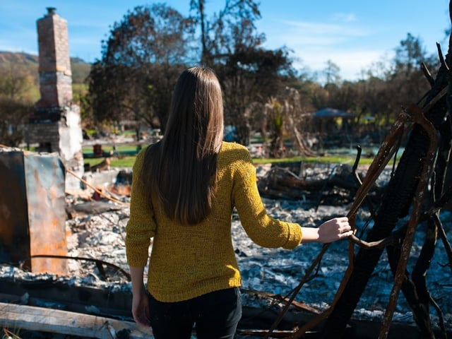 Woman surveying the remains of a home destroyed by a wildfire