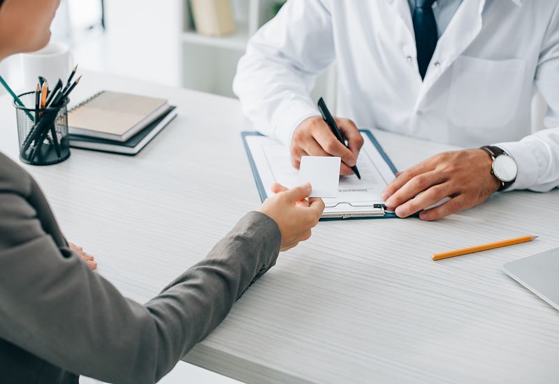 cropped-image-of-patient-giving-id-card-to-doctor-to-fill-insurance-claim-form-in-clinic-800x550
